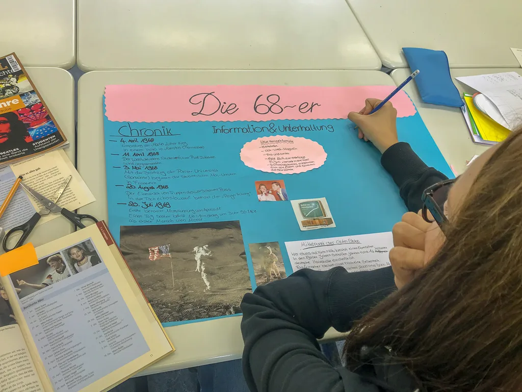 Person beschriftet ein Plakat mit der Überschrift „Die 68er“.